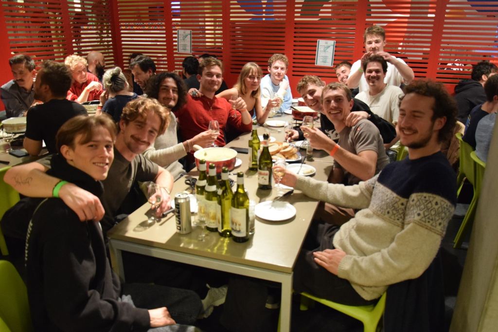 Une tablée d’étudiant·e·s lève son verre autour d’un caquelon pendant la fondue de section
